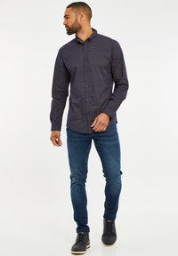 Langärmliges, dunkelblaues Hemd mit einem kleinen weißen Muster, durchgehende Knopfleiste, kombiniert mit dunklen, enganliegenden Jeans und schwarzen Schnürstiefeln.