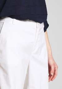 Vita bomullsbyxor med rak skärning, med knappstängning och sidofickor. Bärs med en marinblå strukturerad stickad topp som visar midjeområdet.