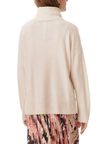 Jasno beżowy sweter z wysokim prążkowanym kołnierzem i detalem w splot kabelkowy na plecach. Luźny krój z prążkowanymi mankietami i dolnym brzegiem.