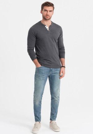 Camisa henley de manga larga gris con una tapeta de tres botones y cuello contrastante, combinada con unos jeans ajustados de corte slim en azul claro y zapatillas beige.