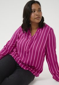 Long-sleeve, V-neck shirt in fuchsia with vertical light pink stripes; soft fabric with a relaxed fit, featuring a single button placket.