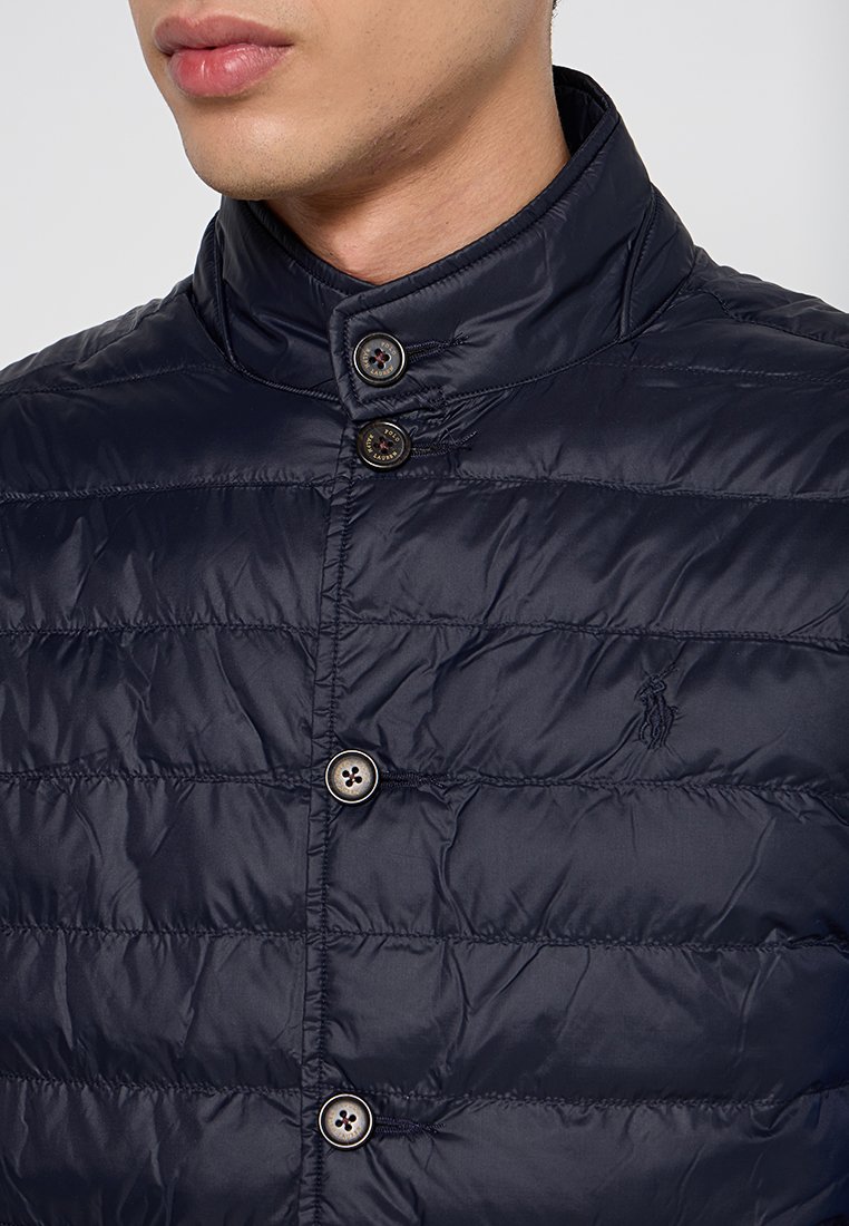 Granatowa pikowana kurtka z wysokim kołnierzem, z trzema guzikami i małym logo. Wykonana z gładkiego, lekkiego materiału.