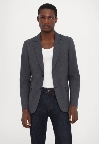 Grau maßgeschneiderte Blazer mit Reverskragen, zwei Knöpfen und Seitentaschen, getragen über einem weißen Tanktop und dunklen Jeans.
