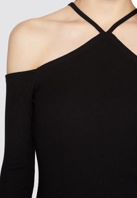 Top preto canelado com uma manga longa e um design de tira cruzada na gola. Textura suave com ligeira elasticidade.