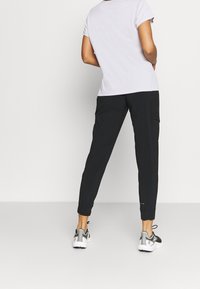 Svarta joggingsbyxor med elastiska muddar, med sidofickor. Kombination med en ljusgrå t-shirt, synlig bakifrån. Sportskor bärs.