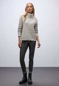 Suéter de punto gris claro con cuello tipo cowl y patrón texturizado, combinado con leggings negros brillantes y botas negras hasta el tobillo.