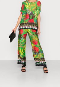 Completo a due pezzi composto da un top a maniche corte e pantaloni a gamba larga, decorato con vivaci motivi verdi e foglie tropicali, rifinito in nero.