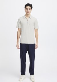 Lys grå kortermet polo med glidelås krage, teksturert mønster, sammen med marineblå bukser og hvite joggesko. Enkel, moderne design.