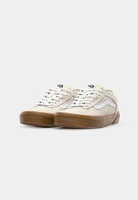 Hvite kanvassneakers med perforert design, brune gummisåler, hvite snører og en hvit stripe detalj på siden.
