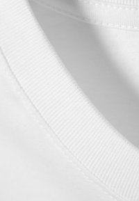 Nahaufnahme eines weißen Baumwoll-T-Shirts mit geripptem Rundhalsausschnitt und glatter Textur. Der Stoff wirkt weich und leicht.
