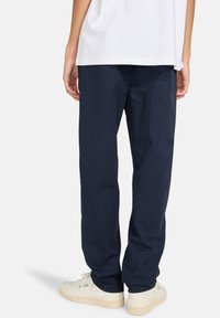 Navy blue, loose-fit pants made from a textured fabric, featuring side pockets and paired with white sneakers.