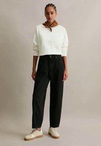 Hvit cropped sweatshirt, høyhåndte svarte bukser og beige sneakers. Brun mønstrete skjerf knyttet rundt halsen. Uformell antrekk.