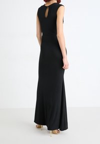 Zwarte maxi jurk met korte mouwen, ronde halslijn en een sleutelgatdetail op de rug. Glad stof met een figuurvormende pasvorm.