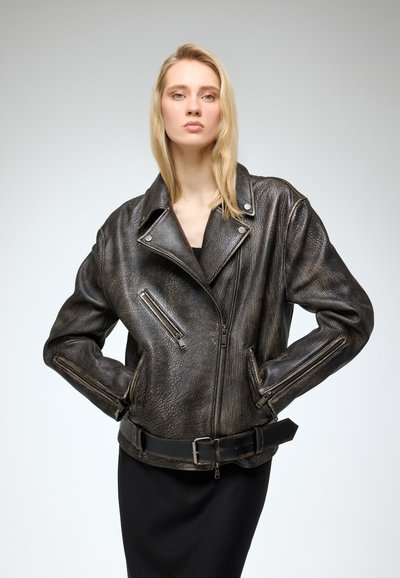 Chaqueta de motociclista de cuero negro con un acabado texturizado, cremallera frontal asimétrica y dos bolsillos con cremallera. Presenta un cinturón ancho en la cintura.