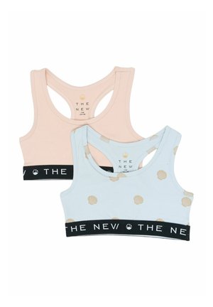 Dwa sportowe biustonosze dla dziewczynek, jeden jasnoróżowy, a drugi jasnoniebieski w nadruk beżowych muszelek, oba z czarnymi elastycznymi paskami z napisem „THE NEW”.