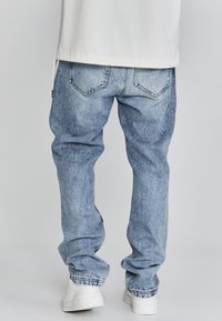 Jeans de mezclilla azul claro con un corte holgado, textura desgastada, bolsillos traseros y bajos doblados, combinados con zapatillas blancas.