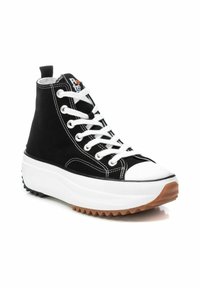 Zapatilla alta de lona negra con cordones blancos, puntera de goma, suela blanca gruesa y suela exterior de goma marrón texturizada. Presenta costuras blancas.