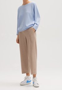 Jasnoniebieski sweter o textured wzorach z szerokim dekoltem, zestawiony z beżowymi spodniami o szerokich nogawkach i białymi sneakersami z niebieskimi akcentami.