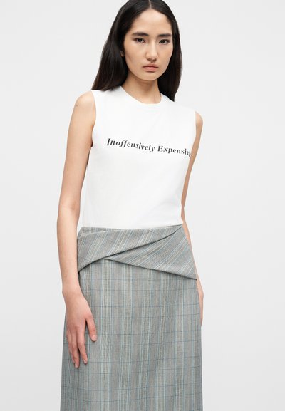 Λευκό αμάνικο μπλουζάκι με μαύρο κείμενο, σε συνδυασμό με γκρι φούστα τύπου wrap με μπλε γραμμές και υφή.
