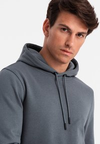 Grijze hoodie met een koord. Zachte stof, lange mouwen, ontspannen pasvorm. Heeft een kangoeroezak en een contrasterende voering in de capuchon.