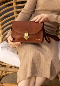 Borsa marrone in pelle sintetica con stampa cocco, dotata di chiusura dorata e tracolla staccabile. Forma rettangolare; texture liscia, branding minimale.