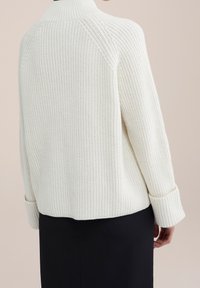 Smetanově zbarvený pletený svetr s vysokým límcem, žebrovanou texturou a širokými manžetami, s volným střihem a raglánovými rukávy.