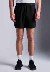 Calções de desporto pretos com um cós elástico. O material é suave e leve. Usados com sapatilhas pretas e meias brancas.