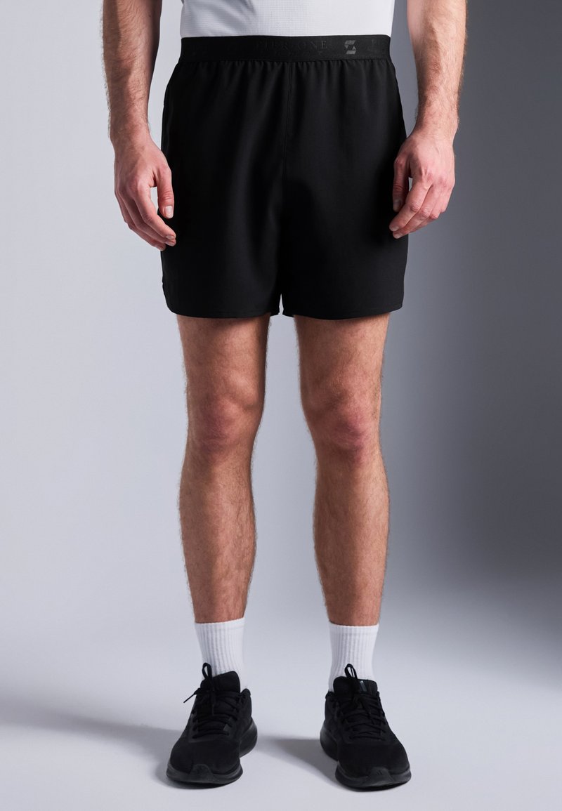 Calções de desporto pretos com um cós elástico. O material é suave e leve. Usados com sapatilhas pretas e meias brancas.