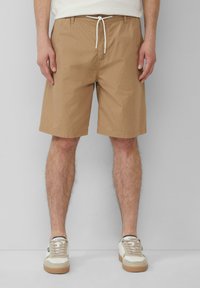 Helle braune Shorts mit Muster, einem Zugbandbund, strukturiertem Stoff und mehreren Taschen, kombiniert mit beigen Sneakers mit hellbraunen Akzenten.