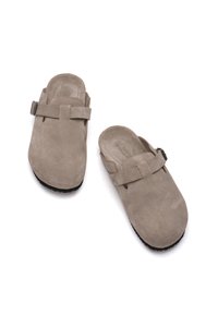 Zoccoli grigi in suede con una punta ampia, una fascia sopra il collo del piede e una suola in gomma nera texturizzata, caratterizzati da un design minimalista e senza motivi.