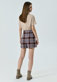 T-shirt beige, pantaloni corti in tartan alta vita bordeaux e blu, tessuto texturizzato, abbinati a stivaletti marroni alla caviglia.
