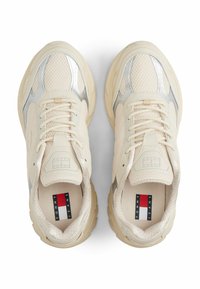 Beżowe i srebrne sneakersy z siateczkowej tkaniny, z amortyzującą podeszwą, sznurówkami oraz logo Tommy Jeans we wnętrzu obszaru pięty, widok z góry.