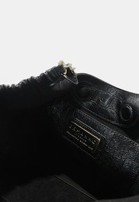 Borsa a mano in pelle nera con superficie texturizzata, hardware dorato, parte superiore arricciata e etichetta interna con testo in rilievo.