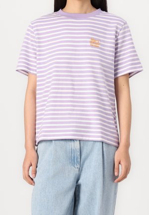 Persona que lleva una camisa de manga corta con rayas lavanda y blancas y unos vaqueros de cintura alta de color azul claro, con las manos relajadas a los lados.