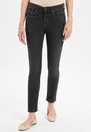 Woman wearing fitted black jeans and beige ballet flats, standing against a plain white background.