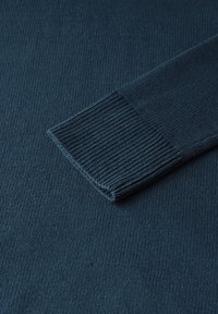 Marineblauw trui stof met een geribbelde textuur. De mouwzoom heeft een sterk ribpatroon en behoudt een over het algemeen gladde uitstraling.