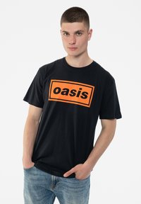 Black cotton t-shirt featuring a large orange rectangular "oasis" logo on the front. Short sleeves and a relaxed fit with a round neckline.