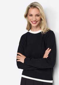 Zwarte longsleeve trui met een witte ronde halslijn en rib gebreide manchetten, met een zachte textuur en een iets cropped ontwerp.