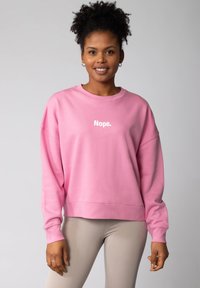 Rosa Sweatshirt mit einem weißen Text-Graphic, das "Nope." liest. Das Sweatshirt hat eine lockere Passform, lange Ärmel, gerippte Bündchen und einen gesäumten Saum.