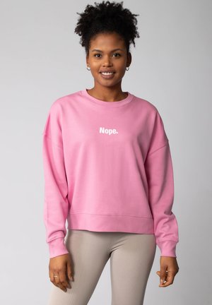 Roze sweatshirt met een witte tekstgraphic met de tekst "Nope." Heeft een relaxed fit, lange mouwen, geribbelde manchetten en een gebande zoom.
