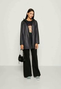 Black leather-style coat with a hood, worn over a graphic t-shirt, paired with black wide-leg pants and checkerboard slip-on shoes.
