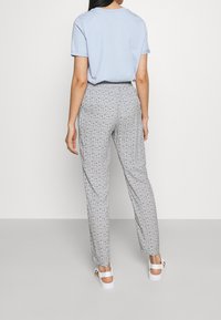 Světle modré tričko ve zkombinování se šedými kalhotami s květinovým vzorem. Oblečení doplňují bílé sandály.