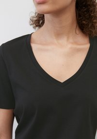 Svart V-hals t-skjorte laget av myk bomull, med korte ermer og en jevn tekstur. Utringningen er definert og litt tettsittende.