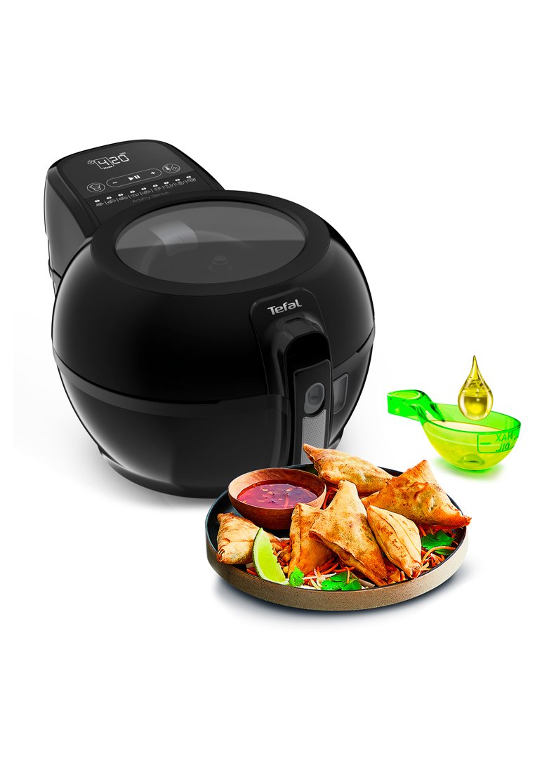 Schwarzer Airfryer mit transparentem Deckel und digitalem Bedienfeld, neben einem Teller mit goldenen Samosas, Dip-Sauce und einem grünen Ölmaß.