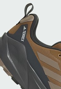 Brown and black sneaker featuring a robust, textured fabric upper, molded heel, and a patterned outsole with gray accents and a pull tab.