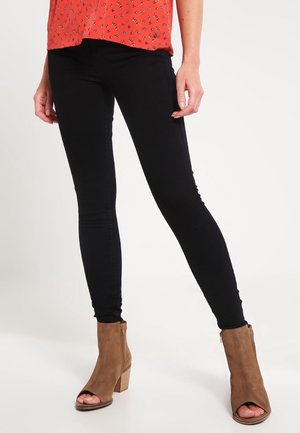 Jeans skinny negros combinados con una blusa roja con estampado floral. Las características incluyen una silueta ajustada y botas de tacón marrón a la altura del tobillo con punta abierta.