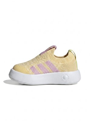 Gelber gestrickter Slip-On-Sneaker mit hellvioletten Streifen, weißer dicker Sohle und Zuglaschen an Ferse und Zunge auf weißem Hintergrund.