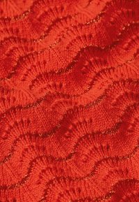 Tejido de punto rojo con un patrón ondulado y acentos de hilo dorado, que muestra textura y profundidad a través de puntos en relieve.
