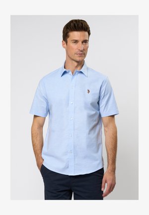 Lühikeste varrukatega helesinine nööbita shirt, mis on valmistatud puuvillast, millel on kerge tekstuur ja väike tikandiga logo vasakul rinnal.