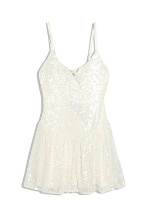 Robe blanche sans manches avec fines bretelles, un petit nœud à l’avant et des ornements en sequins scintillants sur tout le tissu.